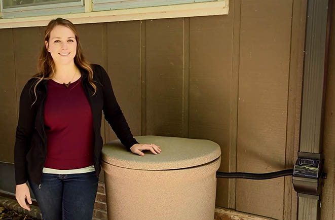how to install a rain barrel, women stands next to a rain barrel outside a home
