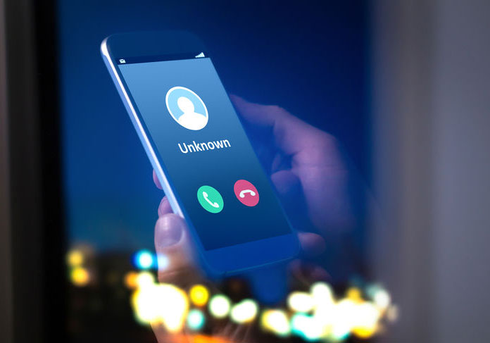 utility scam, a hand holds a smartphone with an unknown caller id on the screen