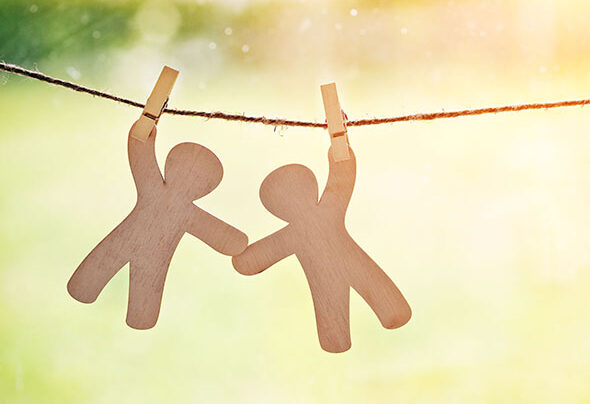 Wooden little men hanging on rope with pin. Symbol of friendship, help, support and emergency assistance.