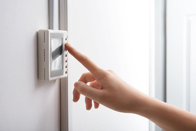 Woman adjusting a smart thermostat on white wall, closeup.